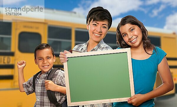 Junge gemischtrassige Schüler mit leerer Kreidetafel in der Nähe des Schulbusses