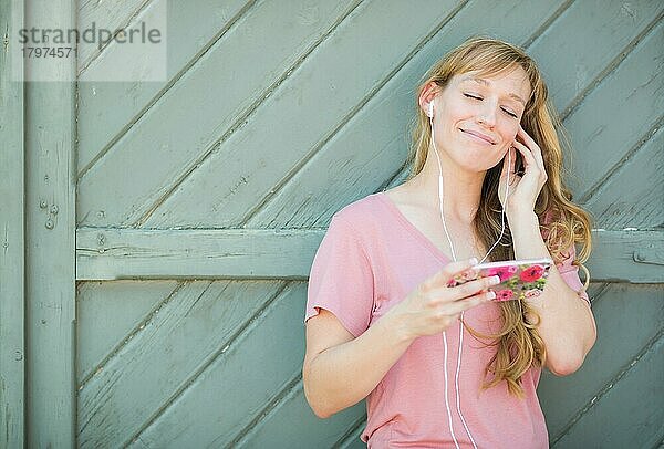 Outdoor-Porträt einer jungen erwachsenen Frau mit braunen Augen  die mit Kopfhörern auf ihrem Smartphone Musik hört