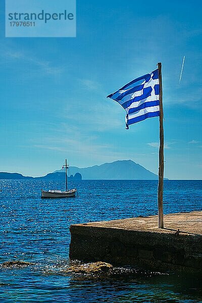 Griechische Flagge in den blauen Himmel auf Pier und traditionellen griechischen Fischerboot in der Ägäis mit griechischen Flagge  Milos Insel  Griechenland  Europa