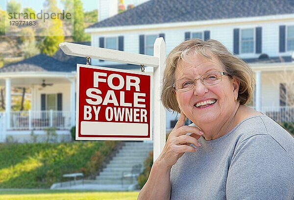 senior woman in front of home for sale by owner real estate sign and beautiful house