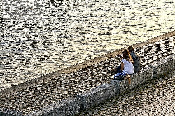 Junges Pärchen sitzt zur Entspannung in der Abendsonne am Spreeufer in Mitte  Berlin  Deutschland  Europa