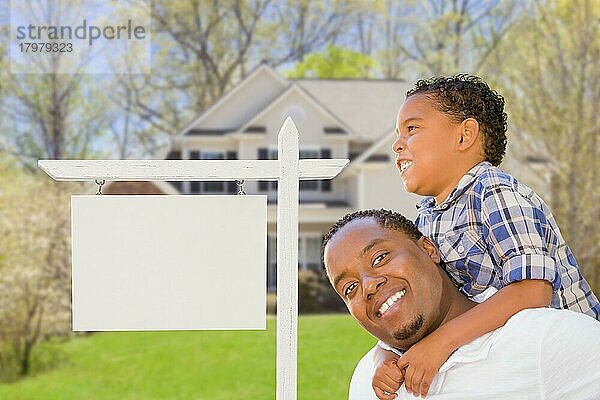 Glücklicher afroamerikanischer Vater und gemischtrassiger Sohn vor einem leeren Immobilienschild und einem neuen Haus