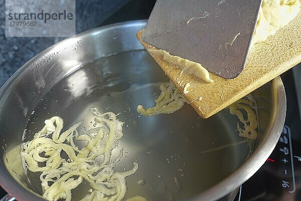 Schwäbische Küche  Zubereitung handgeschabte Spätzle für Spätzle-Auflauf  dreierlei Spätzle  Spätzle klassisch  Mehlspeise  rohen Teig in kochendes Wasser schaben  Spätzleschaber  Spätzlebrett  Kochtopf  Indiktionsherd  Ceranfeld  typisch Schwäbisch  Traditionsküche  vegetarisch  Foodfotografie  Studio  Deutschland  Europa