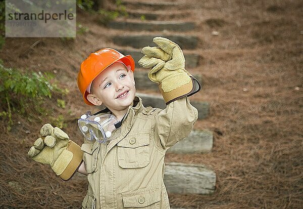 Glücklich adorable Kind Junge mit großen Handschuhen  harten Hut und Schutzbrille spielen Handwerker draußen