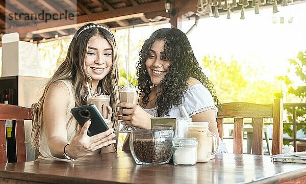 Zwei Mädchen machen ein Selfie und trinken Kaffee  zwei Freundinnen mit dem Handy in einem Café