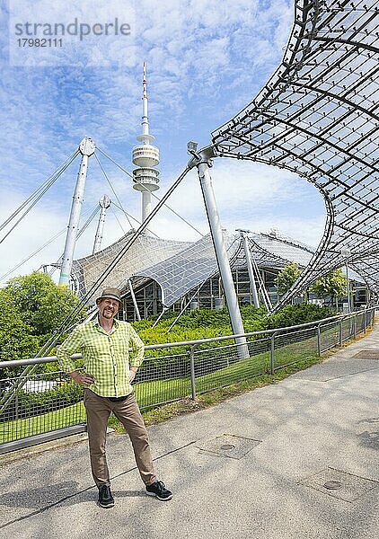 Freundlich lächelnder Mann beim Olympiaturm mit Olympia-Zeltdach  Olympiapark  Olympiagelände  München  Oberbayern  Bayern  Deutschland  Europa