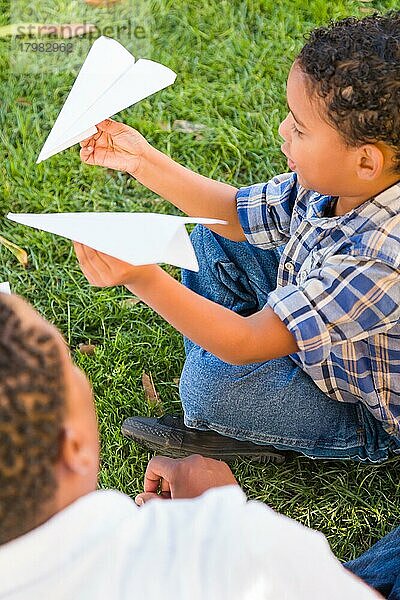 Glücklicher afroamerikanischer Vater und gemischtrassiger Sohn spielen mit Papierflugzeugen im Park