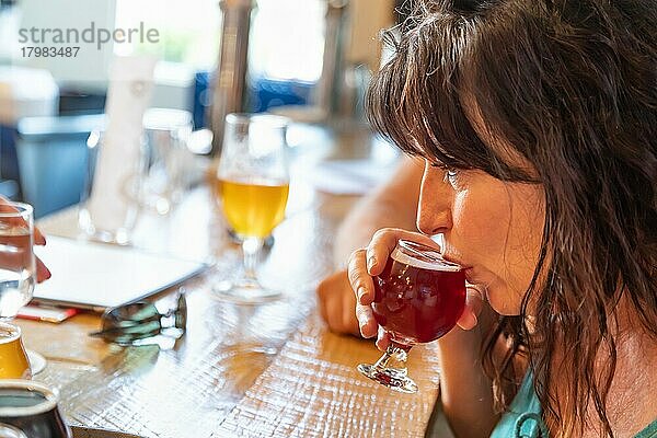 Frau nippt an einem Glas Mikrobrau-Bier in einer Bar mit Freunden