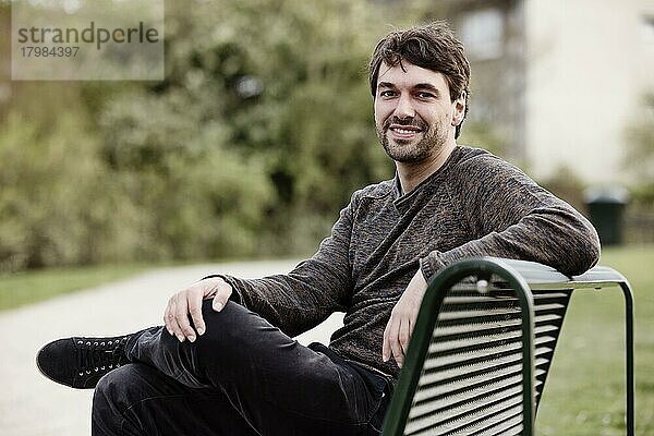 Junger Mann draußen auf einer Parkbank sitzend  Portrait  Köln  Nordrhein-Westfalen  Deutschland  Europa