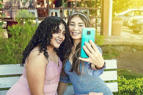 Zwei hübsche Mädchen sitzen auf einer Bank und machen ein Selfie  Mädchen lächeln und machen ein Selfie