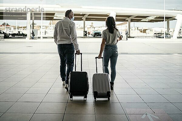 Ein paar Freunde mit Gepäck und Schutzmasken verlassen den Flughafen