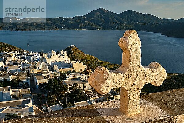 Griechisch-Orthodoxes Christentum Konzept Hintergrund  Fokus Blumen  christliche Kreuz mit Plaka Dorf auf Milos Insel im Hintergrund auf Sonnenuntergang  Plaka Stadt  Milos Insel  Griechenland  Europa