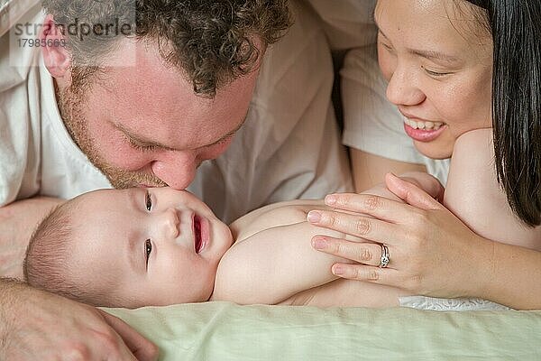 Gemischtrassiges chinesisches und kaukasisches Baby  das mit seinem Vater und seiner Mutter im Bett liegt