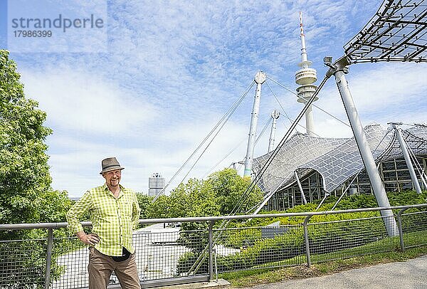 Freundliche lächelnder Mann beim Olympiaturm mit Olympia-Zeltdach  links BMW-Turm  Olympiapark  Olympiagelände  München  Oberbayern  Bayern  Deutschland  Europa