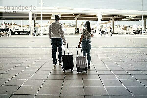 Ein paar Freunde mit Gepäck und Schutzmasken verlassen den Flughafen