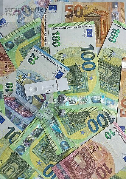 Geld (Euro-Banknoten) mit Antigentest  Impfstoffflaschen und Spritze. Finanzkrise aufgrund von Coronavirus-Verlusten  selektiver Fokus