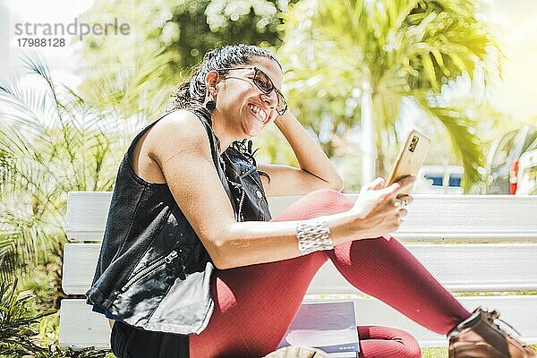 Mädchen sitzt auf einer Bank und überprüft ihr Handy  Glückliche Frau sitzt in einem Park und schreibt eine SMS auf ihrem Handy  Glückliche Frau sitzt auf einer Bank und schickt eine SMS