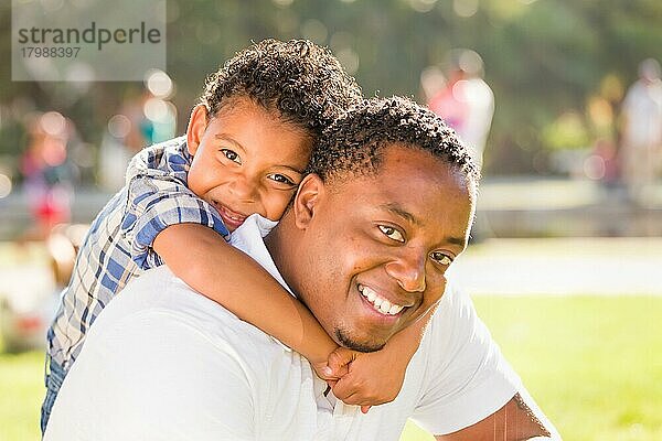 Glücklicher afroamerikanischer Vater und gemischtrassiger Sohn spielen im Park