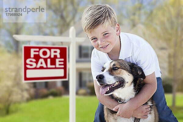 Glücklicher Junge und sein Hund vor einem zu verkaufenden Immobilienschild und Haus