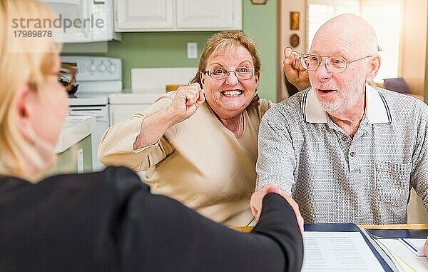 Älteres erwachsenes Paar  das mit einem Agenten bei der Unterzeichnung von Dokumenten in seiner Wohnung feiert