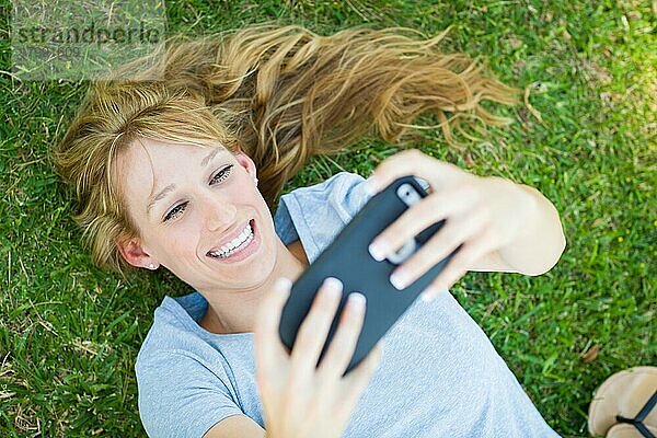 Junge erwachsene Frau liegt im Gras und macht ein Selfie mit ihrem Smartphone