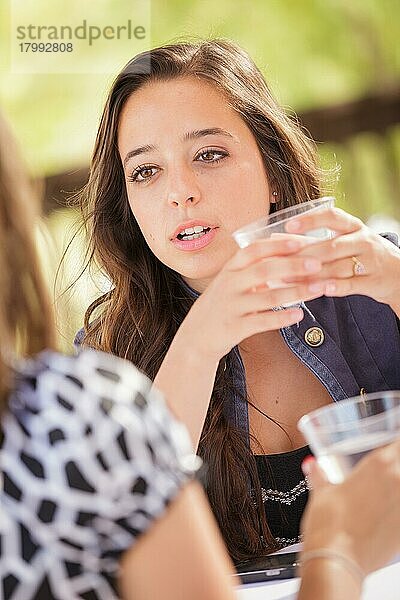 Ausdrucksstarke junge erwachsene Frau  die im Freien etwas trinkt und sich mit ihrer Freundin unterhält