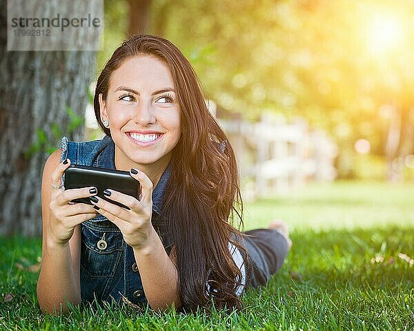 Attraktive  glückliche  gemischtrassige junge Frau  die draußen im Gras liegt und mit ihrem Handy telefoniert