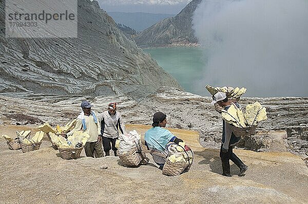 Einheimischer Mann mit Schwefelblöcken in Körben  der sich auf dem Pfad um den Vulkankrater herum ausruht  in der Nähe des türkisgrün gefärbten sauren Vulkankratersees  Mount Ijen  Ostjava  Indonesien  Asien