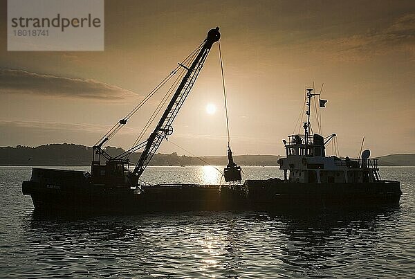 Bagger bei der Arbeit  Ausbaggern des Hafens einer Küstenstadt  Silhouette bei Sonnenuntergang  Padstow  Cornwall  England  April