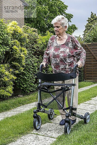 Ältere Frau mit Rollator  Rollator übt das Gehen auf der Auffahrt zu Hause