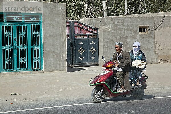 Uigurischer Mann in traditioneller muslimischer Kleidung  Kind und Frau mit islamischem Schleier fahren auf einem Motorroller  Xinjiang  China  Asien