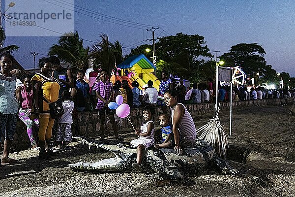 Mutter und zwei Kinder posieren auf künstlichem Krokodil  Attrappe  Pappmaché  Volksfest  Dämmerung  Mahajanga  Madagaskar  Afrika