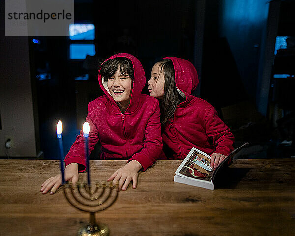 Zwei glückliche Kinder sitzen am Tisch mit Hannukah-Kerzen