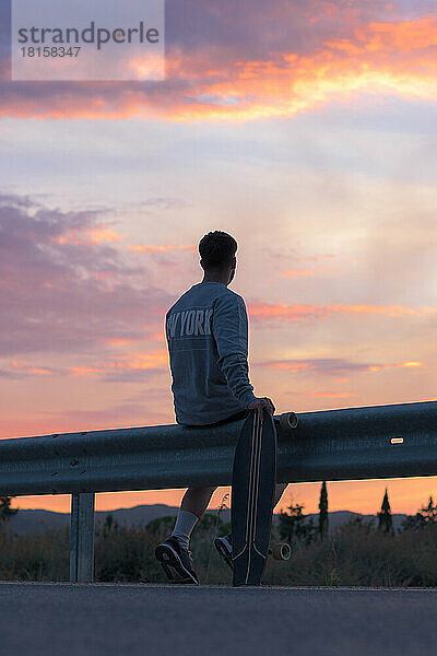 Ein junger Mann auf einem Skateboard schaut in den Sonnenuntergang hinaus