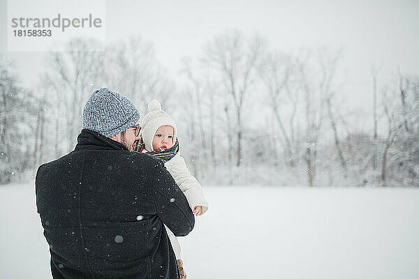 30-jähriger kaukasischer Vater hält einen Jungen kleinen auf einem verschneiten Feld.