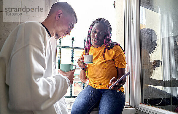 Glückliches multiethnisches Paar trinkt Kaffee und benutzt dabei seine Mobiltelefone