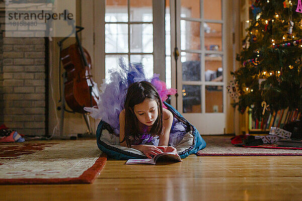 Ein kleines Mädchen im Tutu liegt auf dem Boden neben dem Weihnachtsbaum