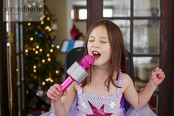 Ein kleines Mädchen im Kostüm singt zu Hause laut in einem Mikrofon