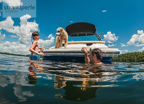 Mann und Kind schwimmen an einem Sommertag von der Rückseite eines Bootes.