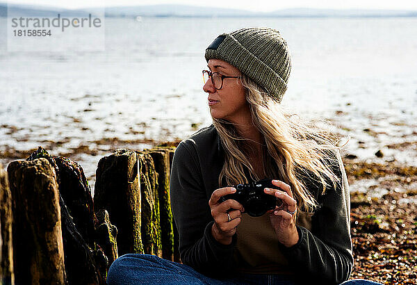 Nachdenklich blickende Frau beim Fotografieren am Strand