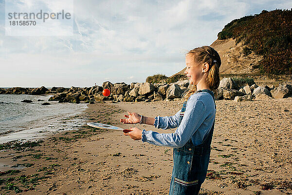 Mädchen spielt am Strand fröhlich mit Schläger und Ball