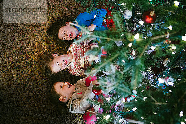 Geschwister lachen und lächeln unter der Weihnachtsbaumbeleuchtung