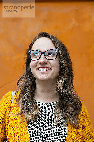 Ein Mädchen mit Brille auf einem orangefarbenen Hintergrund lächelt