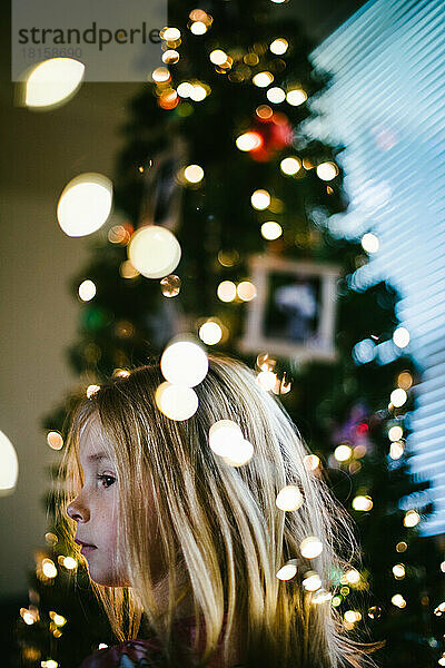 Blondes Mädchen vor Weihnachtsbaum mit Lichtern und Ornamenten