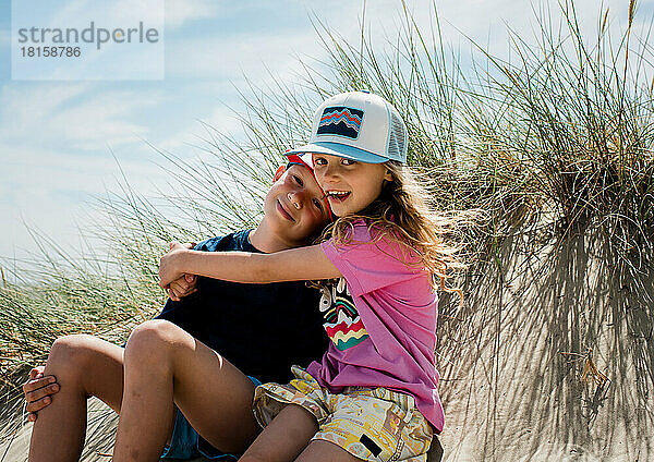 Geschwister  die sich an einem sonnigen Tag im Urlaub am Strand umarmen