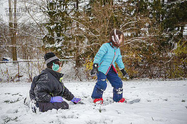 Ein Junge bringt seine kleine Schwester im Winter das Snowboardfahren bei