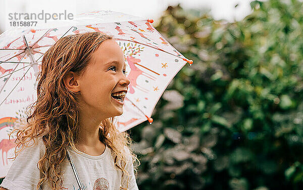 Mädchen lacht und hält einen Regenschirm im Regen