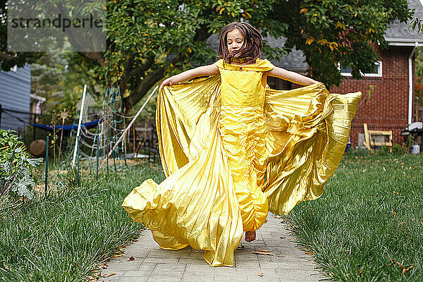 Ein Mädchen in goldenem Kleid und Flügeln springt barfuß in die Luft im Hinterhof