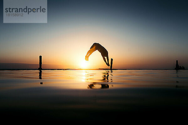 Silhouette eines jungen Mannes  der bei Sonnenuntergang in den Pool springt