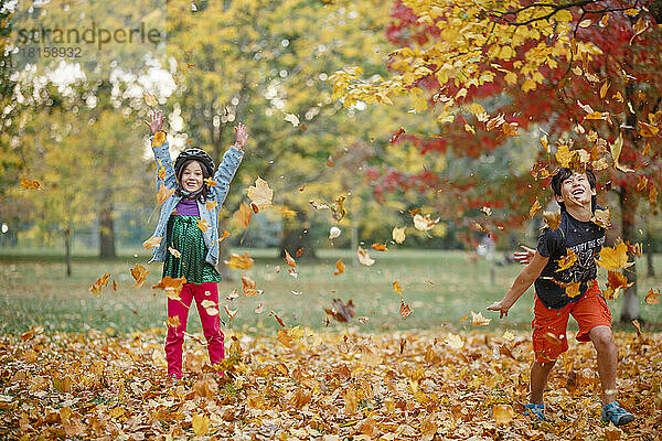 Zwei glückliche Kinder spielen zusammen in einem Haufen Herbstblätter